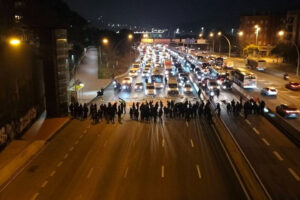 il fait nuit, une autoroute est bloquée par un cinquantaine ou centaine de personnes avec des banderoles. des voitures attendent, phares allumés.